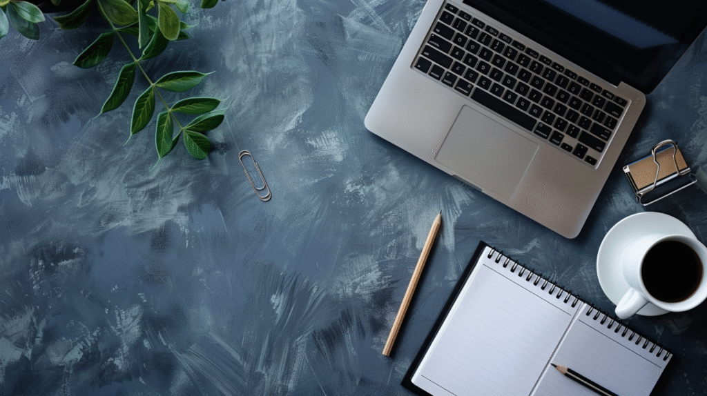 Flacher Schreibtisch mit Laptop, Notizbuch, Kaffeetasse und Pflanze – kreative Arbeitsatmosphäre im Homeoffice.