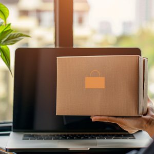 Karton mit Lieferlogo vor Laptop – symbolische Darstellung digitaler Übergabe.